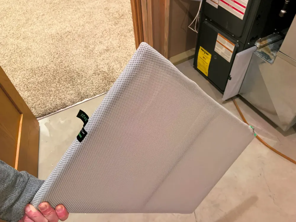 A person holding a large mesh HVAC air filter next to a furnace